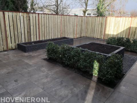 Tuinaanleg met siertegels, plantenbakken en houten schutting