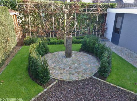 Tuin met leibomen en zonnewijzer op terras van gekleurde koppelstenen