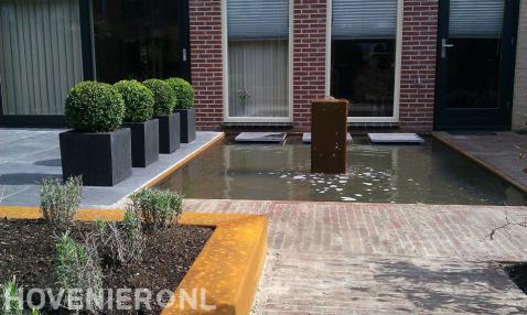 Terras met buxusbollen in plantenbakken bij vijver met waterornament