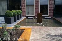 Terras met buxusbollen in plantenbakken bij vijver met waterornament