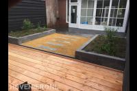 Achtertuin met bestrating, plantenbakken en houten vlonder