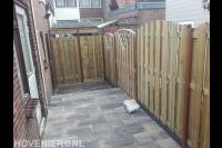 Nieuwe bestrating met siertegels en houten schutting met poort