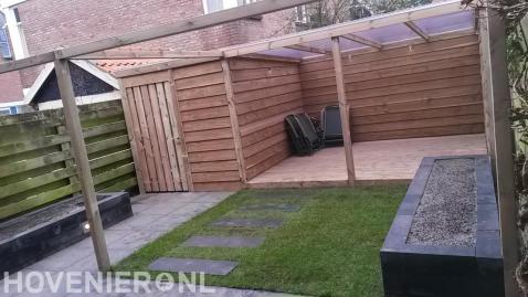 Achtertuin met klein gazon, pergola en houten berging met overkapping