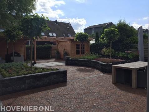 Tuin met bestrating, plantenbakken en houten schuurtje met pergola