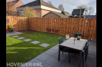 Tuinaanleg met sierbestrating, kunstgras en houten schutting