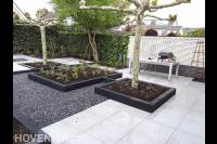 Moderne achtertuin met grote tegels, kiezels en plantenbakken