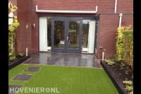 Strakke achtertuin met antraciet tuintegels en kunstgras