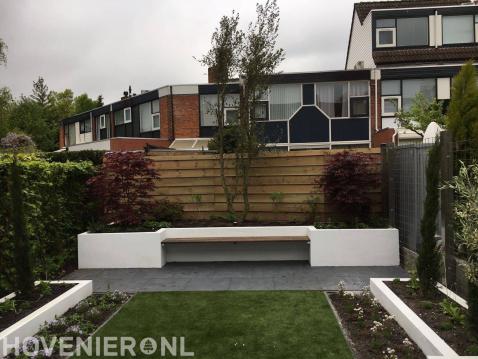 Moderne achtertuin met kunstgras, witte plantenbakken en zitbankje 1