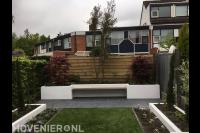 Moderne achtertuin met kunstgras, witte plantenbakken en zitbankje 1