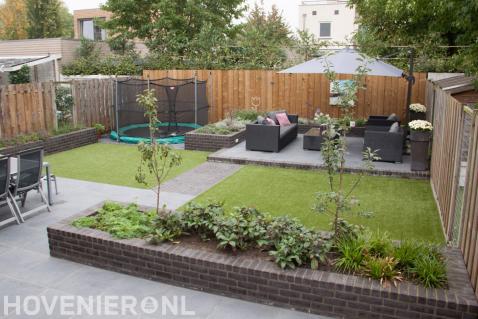 Strakke achtertuin met gazon en terras met loungeset en parasol