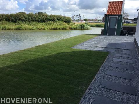 Tuin aan het water met gazon en sierbestrating