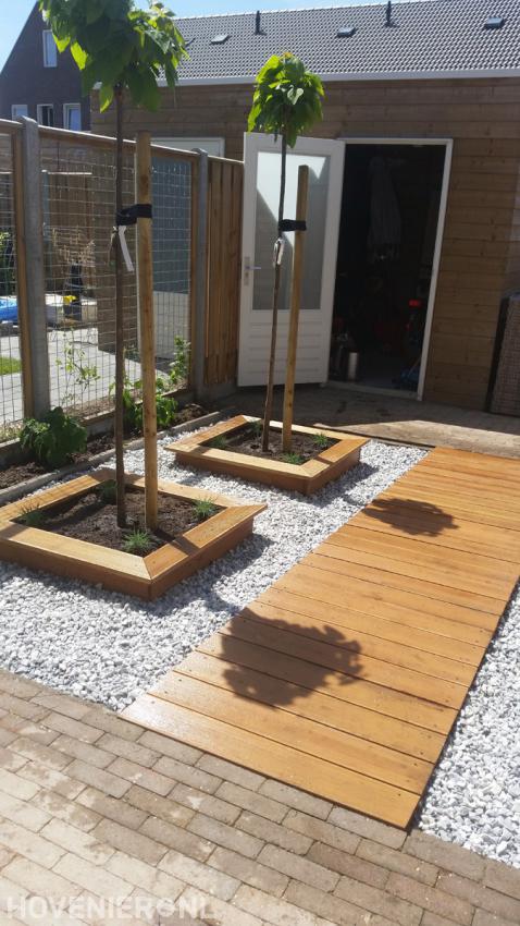 Tuin met vlonder, grind en houten plantenbakken met boompjes