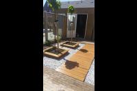 Tuin met vlonder, grind en houten plantenbakken met boompjes