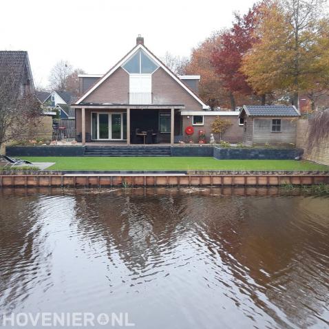 Tuin aan het water met beschoeiing, kunstgras en verhoogd terras