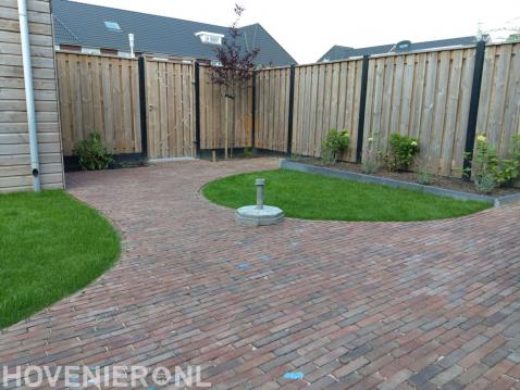 Achtertuin met sierbestrating, grasmatten en beton houtschutting