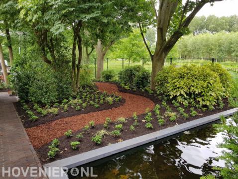 Tuin met vijver, veel groen en looppad van boomschors