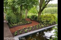 Tuin met vijver, veel groen en looppad van boomschors