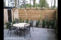Achtertuin met terras en pergola en houten schutting