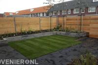 Achtertuin met betontegels, graszoden, plantenbakken en schutting