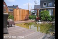 Tuin met heldere vijver, vlonder en houten schutting met betongaas