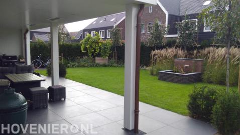 Tuin met terras van keramische tegels, gazon en kleine vijver