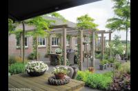 Tuin met grote houten pergola boven terras en veel groen 1