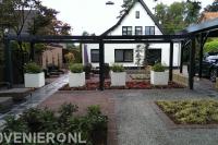 Moderne tuin met grote pergola van donker hout en witte bloembakken