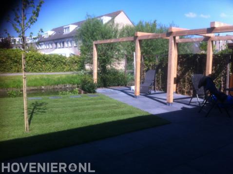 Robuuste houten pergola boven terras van antraciet tuintegels