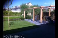 Robuuste houten pergola boven terras van antraciet tuintegels