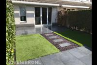 Achtertuin met natuursteen tegels en kunstgras