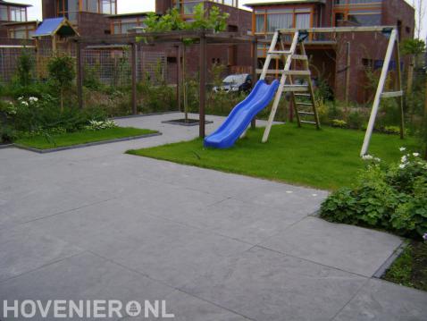 Tuinaanleg met sierbestrating, gazon, houten pergola en speeltoestel