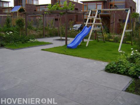 Tuinaanleg met sierbestrating, gazon, houten pergola en speeltoestel