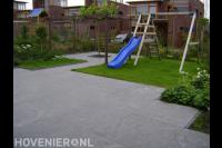 Tuinaanleg met sierbestrating, gazon, houten pergola en speeltoestel