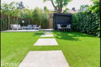 Gazon met stapstenen en zithoek met loungeset bij tuinhuisje