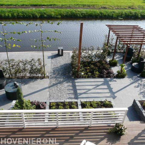 Moderne tuin aan het water met bestrating, pergola en leibomen 1