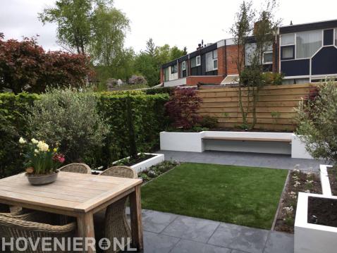Moderne achtertuin met kunstgras, witte plantenbakken en zitbankje 2
