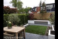 Moderne achtertuin met kunstgras, witte plantenbakken en zitbankje 2