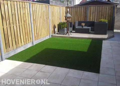 Tuin met vlonder, kunstgras, bestrating en houten schutting