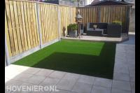 Tuin met vlonder, kunstgras, bestrating en houten schutting
