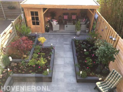 Tuin met bestrating, plantenbakken en houten overkapping met berging