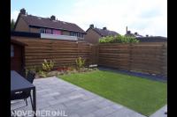 Strakke achtertuin met bestrating, kunstgras en houten schutting