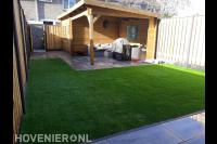 Achtertuin met bestrating, kunstgras en houten overkapping met berging