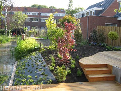 Tuin aan het water met nieuwe beplanting en houten vlonder met trap