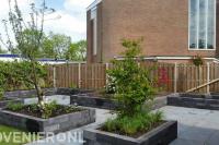 Strakke tuin met plantenbakken van stapelblokken en houten schutting