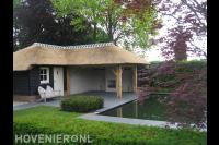 Schuurtje met overkapping en rieten dak bij vijver