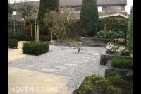 Achtertuin met natuursteentegels in basaltgrind en verhoogde borders