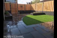 Tuinaanleg met bestrating, plantenbakken, kunstgras en schutting