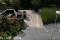 Stenen trap naar houten vlonder met loungeset aan het water