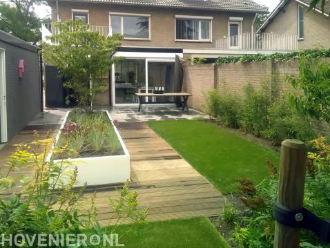 Moderne tuin met terras, kunstgras, vlonder en witte plantenbak