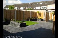 Achtertuin met kunstgras, borders van stapelblokken en grote tegels